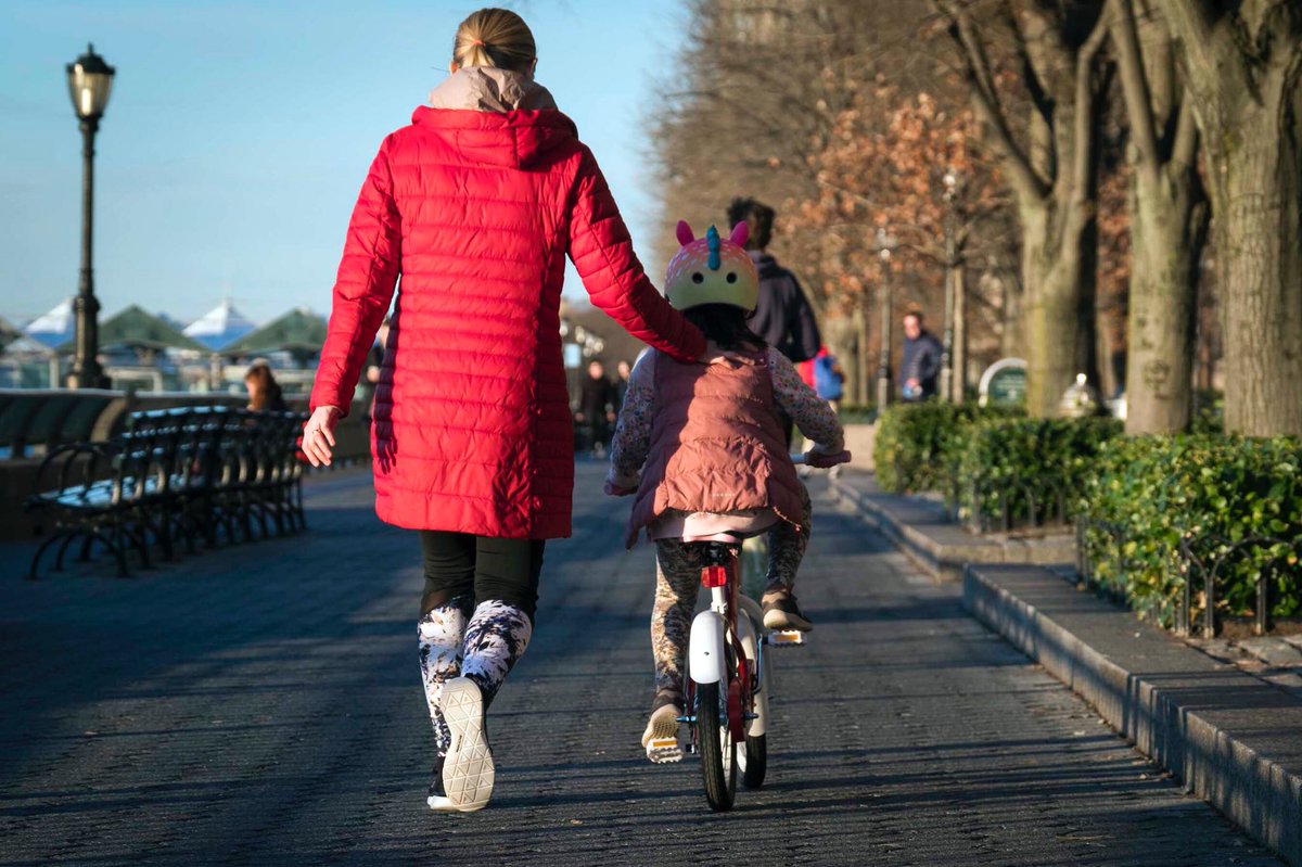 A photo of a woman guiding a child along on a bike.
