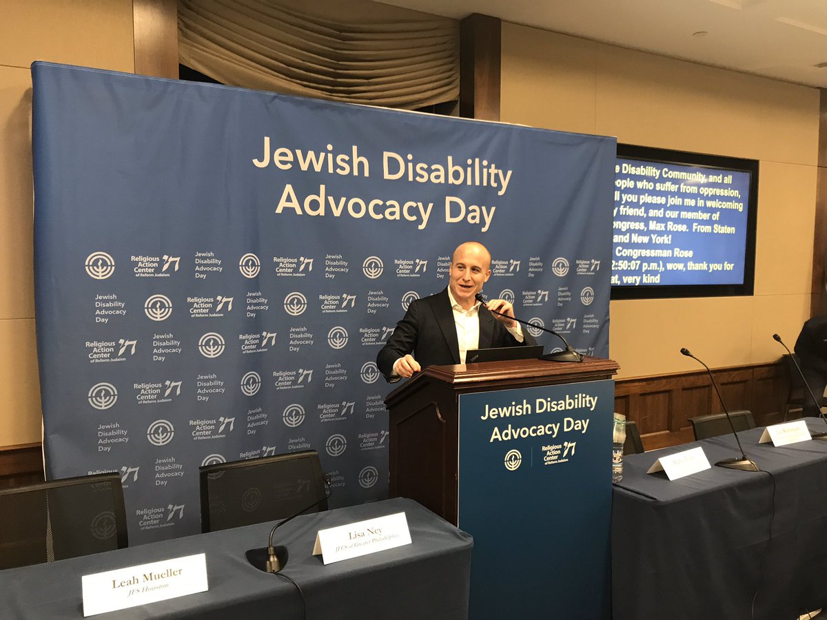 Rep. Max Rose stands at a podium with empty tables on either side and addresses the JDAD audience