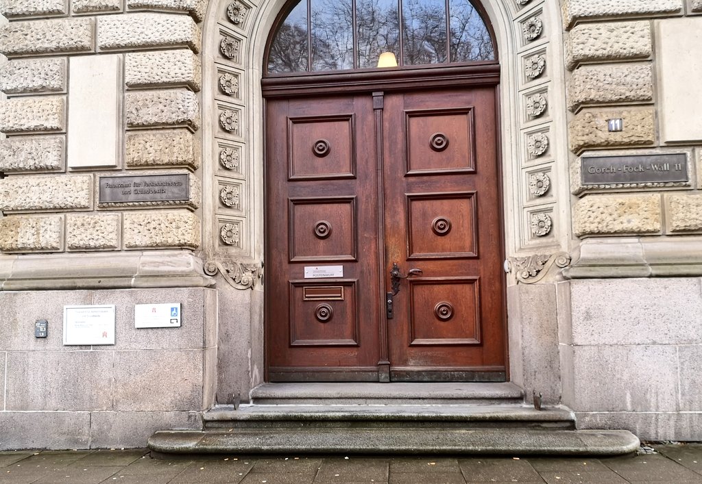 Drei Stuffen zur  Tür des Finanzamtes mit Briefeinwurfschlitz und Hinweisschild auf rückwärtigen Behinderteneingang .