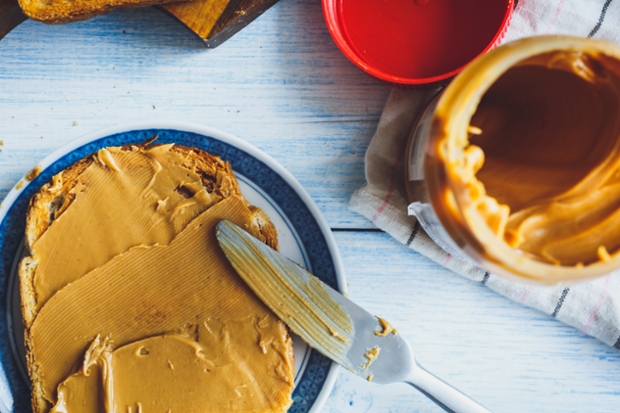 An overhead shot of a piece of bread with peanut butter spread onto of it. Beside it is an open jar of peanut butter. 