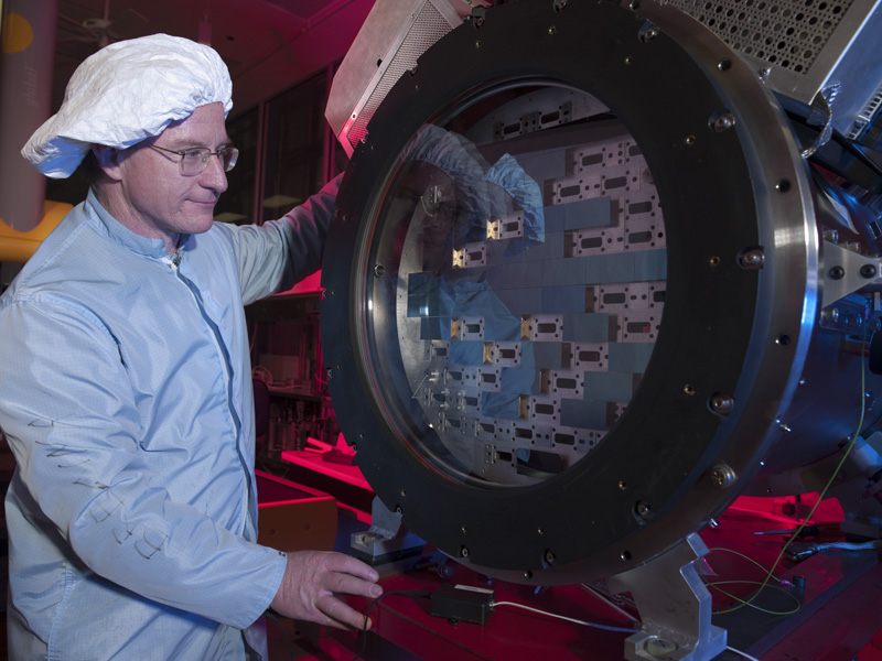A person in a blue coverall and hair net looking at a piece of the DES camera.