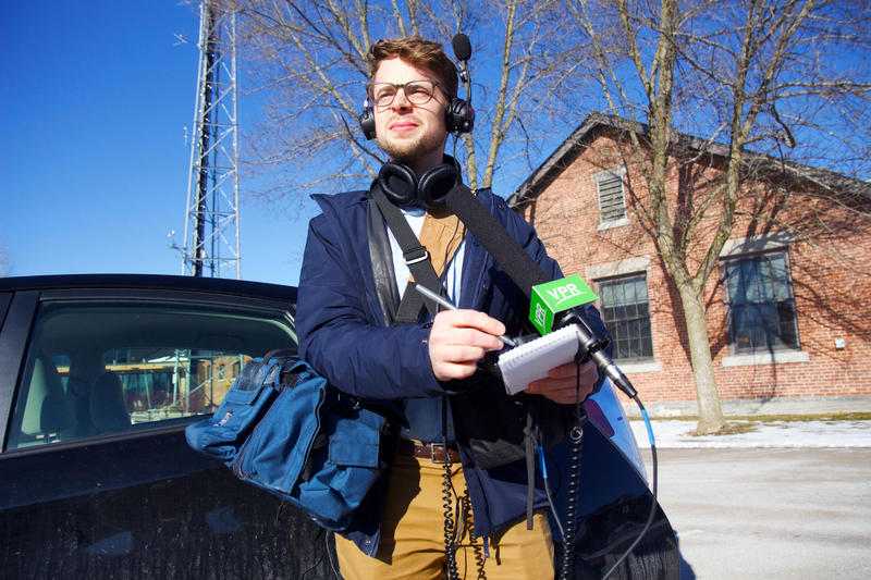 Henry Epp wears an absurd amount of gear including headphones, camera bags, a notepad and microphone.