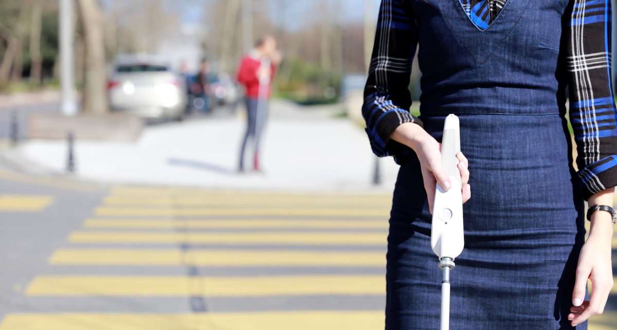 A woman uses a WeWalk smart cane as she cross the road