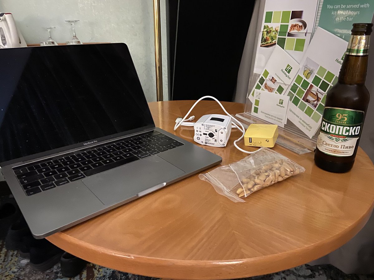 Laptop on hotel room table with peanuts and a bottle of beer