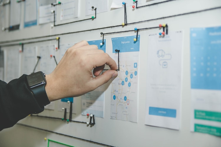 person working on a whiteboard with blue and white papers pinned to it
