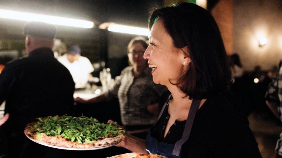 Ann Kim holding two pizza pies, as though to serve them, and smiling.