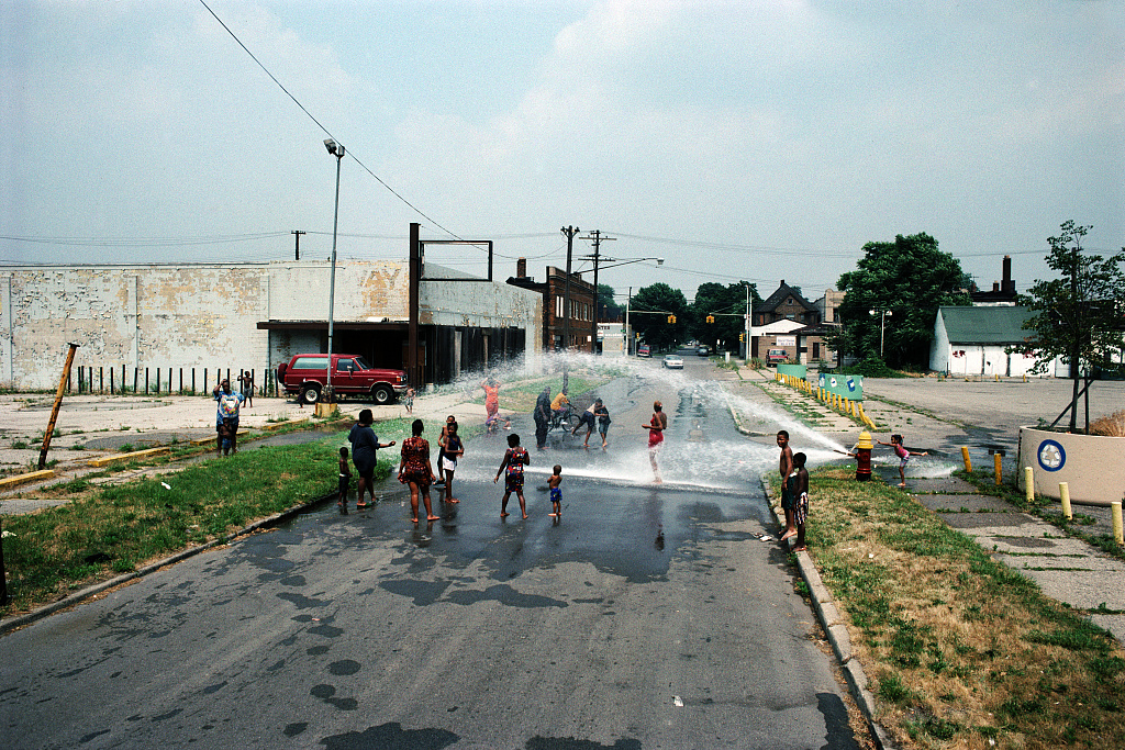 kids in street playing with open fire hose