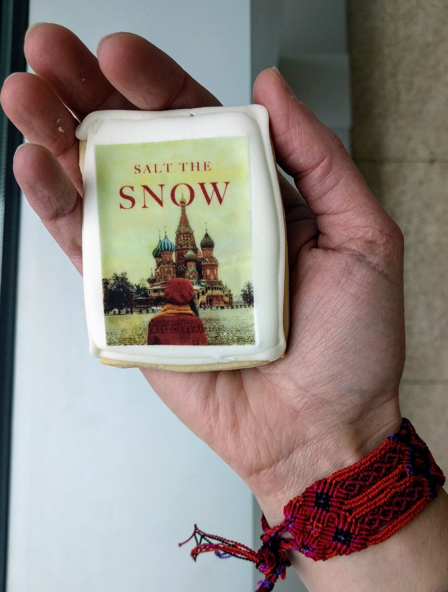 My hand holding a rectangular cookie with the Salt the Snow cover (a woman facing a Russian church)
