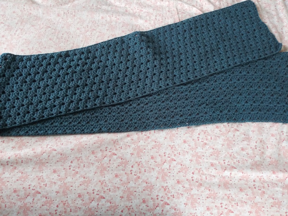 A dark teal scarf folded in half on a pastel pink background