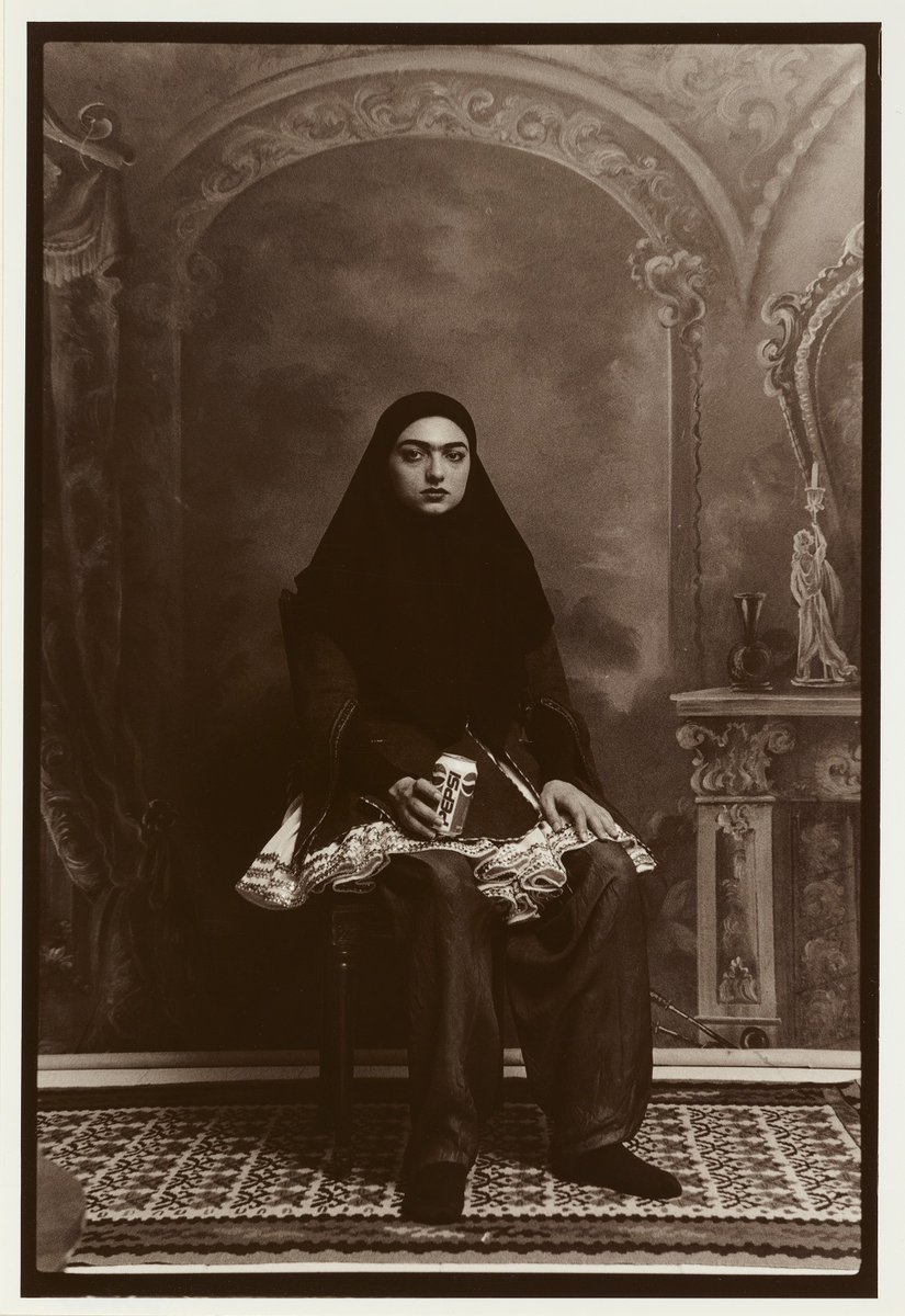 Woman in hijab, holding a Pepsi can, sitting on chair.