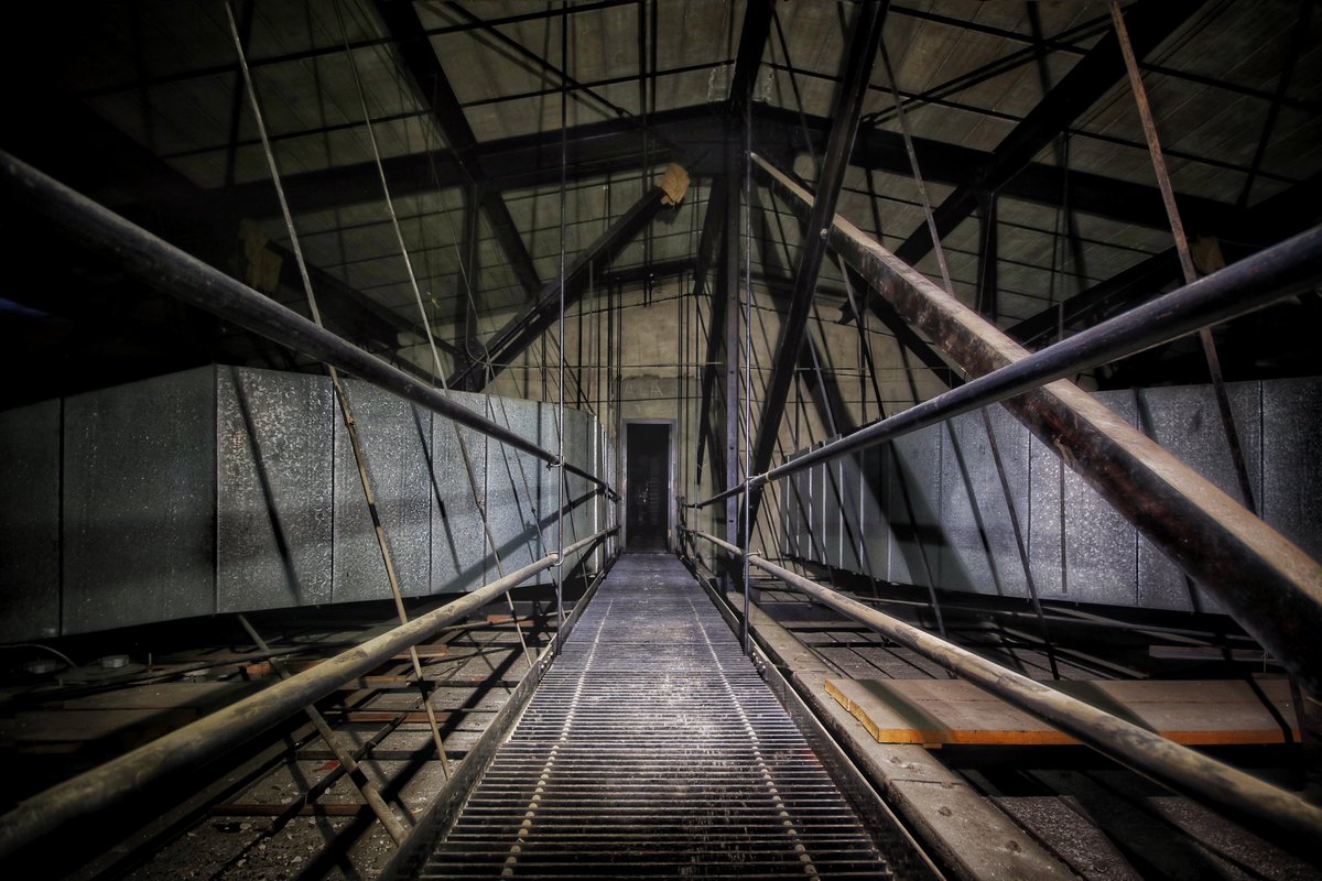 A view down the long, dark catwalk at the Worcester Memorial Auditorium. Black steel rods branch out of the central walkway like spider legs.