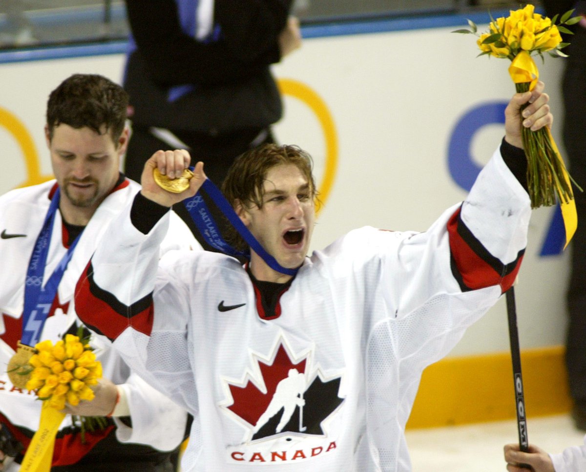 Ryan holds his medal up in one hand and flowers in the other.