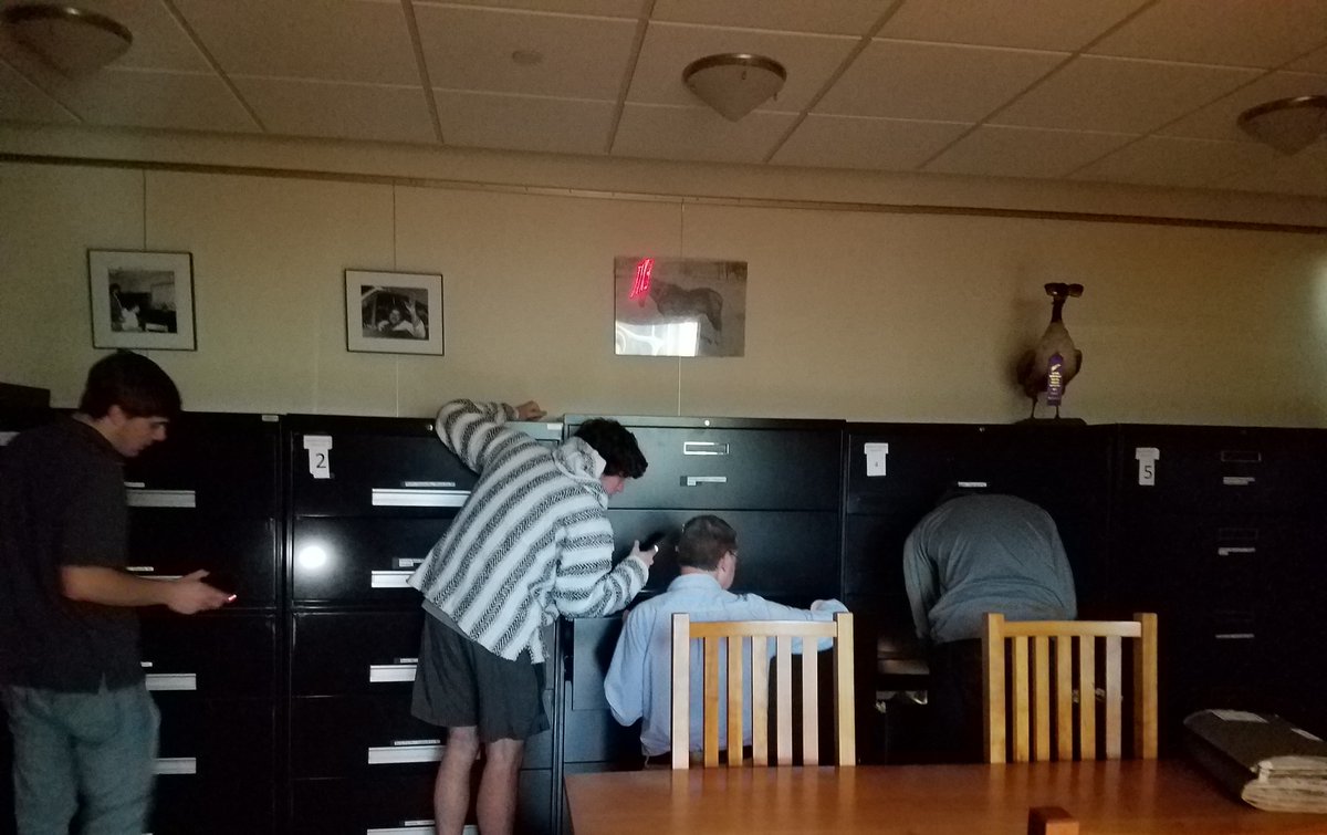 Students and staff search for newspaper clippings files with the help of their phone flashlights.