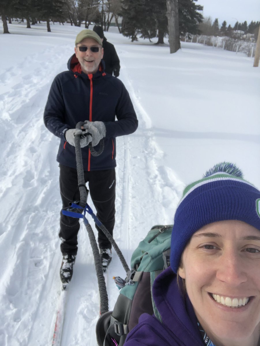 Two people cross country skiing, one being towed by the other