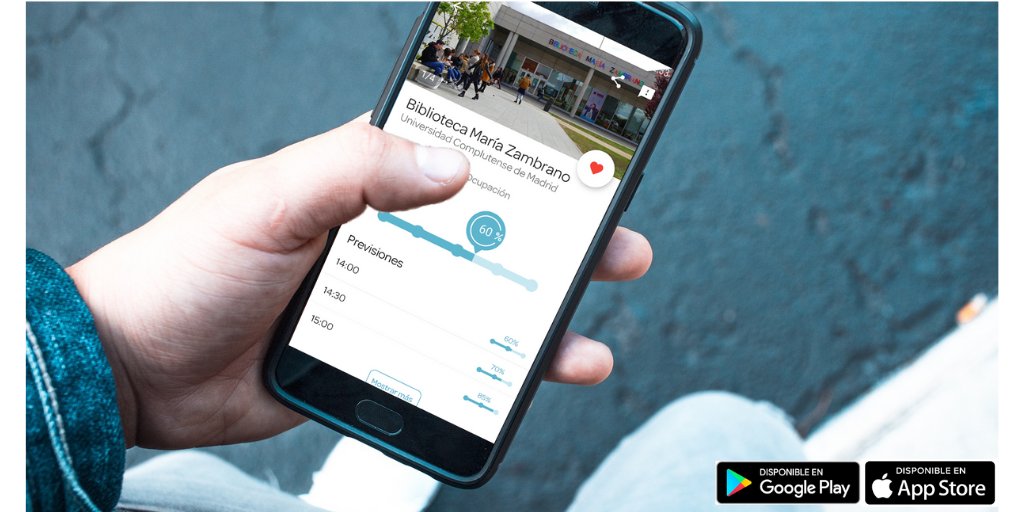 Una mano sujeta un teléfono móvil en cuya pantalla se puede ver la información de la biblioteca María Zambrano en la App Affluences: el porcentaje de ocupación por horas y una foto de la la entrada de la Zambrano