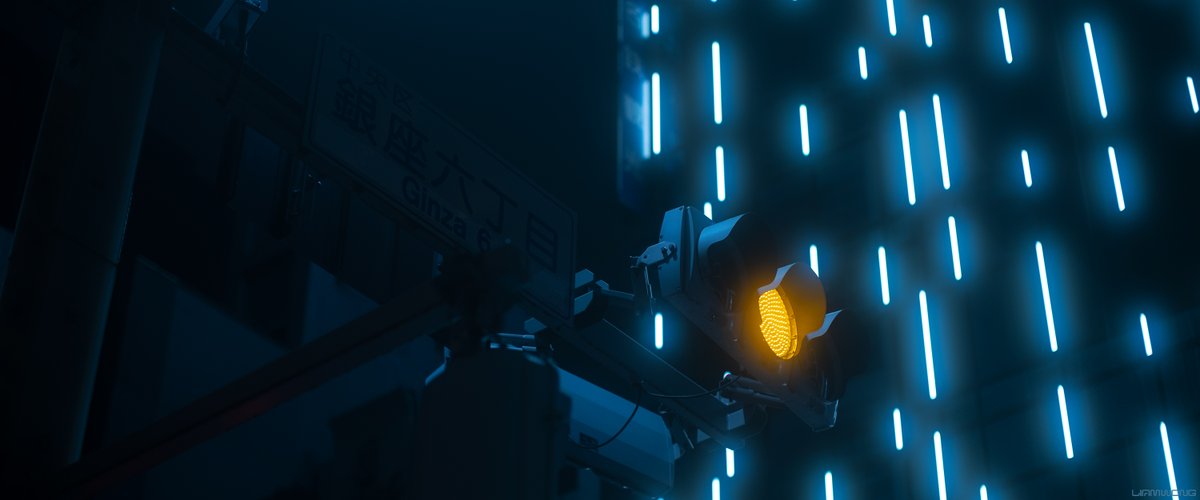 Photography by Liam Wong of Tokyo at night in the Ginza district. A traffic light and highway sign which reads 'GINZA'. The light is yellow and is glowing. In the background are the rain-like neon light strips which are hazy with a light blue tint.