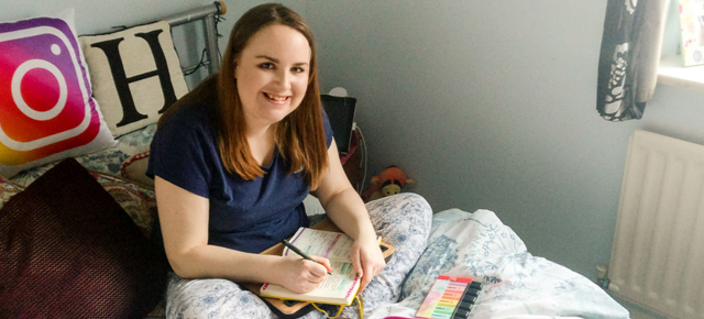 image shows Hannah sat on her bed.