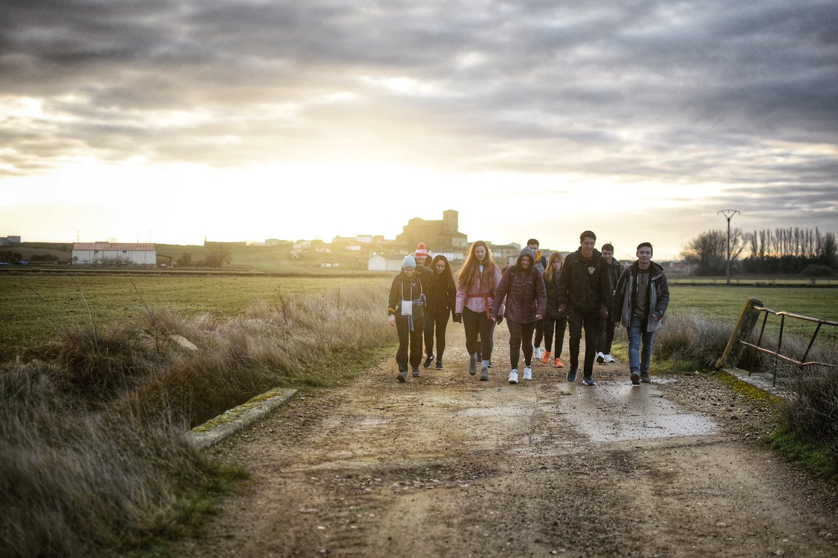 Students walk along a dirt road with a silhouetted Spanish castle behind them.