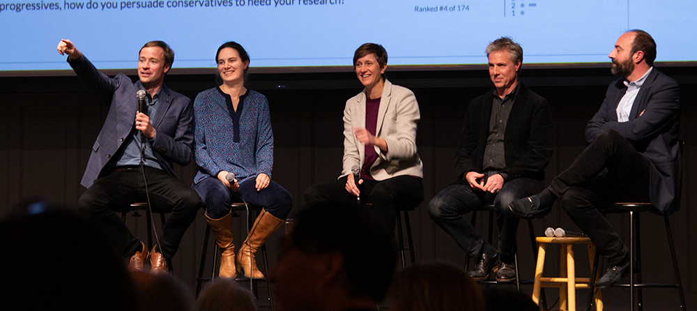 Seated with four other panelists, Jevin West points to an attendee
