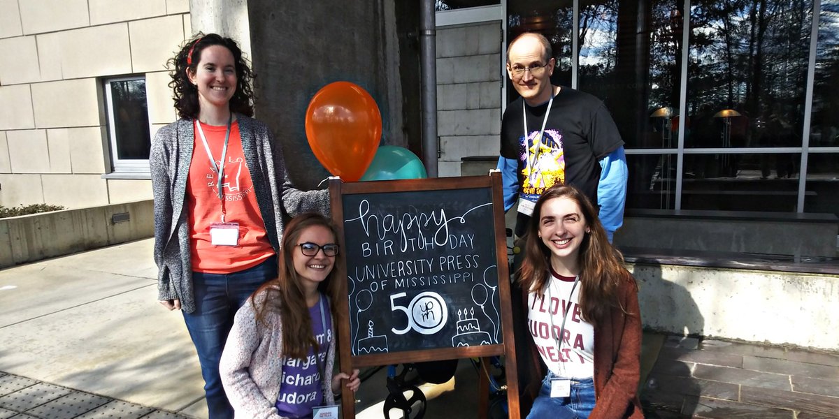 Four UPM employees stand in front of a side wishing happy birthday to the University Press of Mississippi
