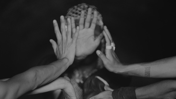 A black-and-white still from Luiz Roque's film "S" which depicts a number of hands obscuring a figure's face.