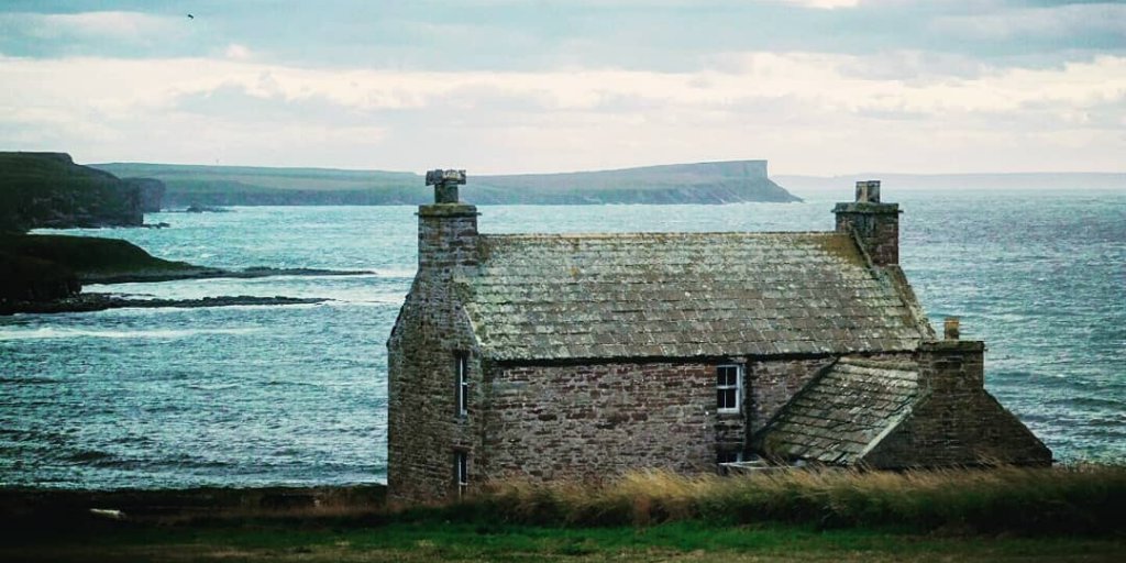View of the coast in Orkney with stone farmhouse in foreground