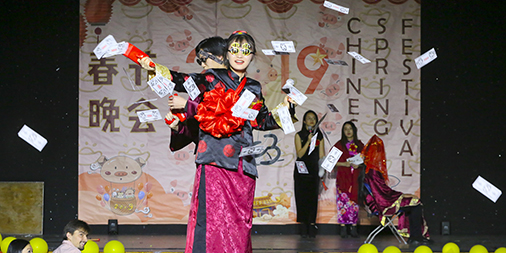 students on stage in traditional outfits throw fake money into the air to celebrate Lunar New Year