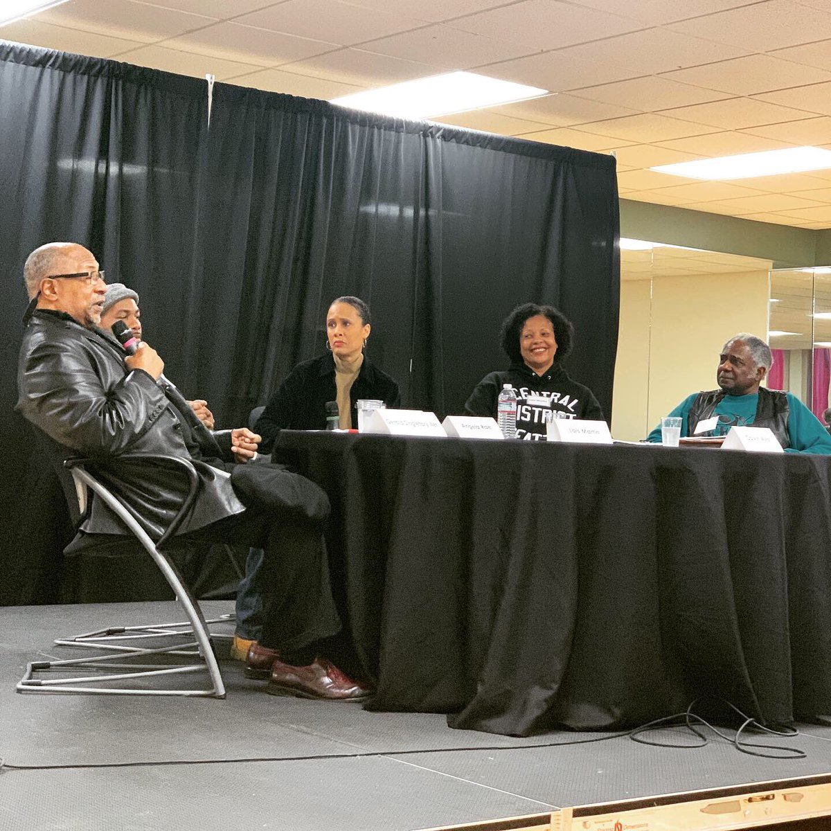 Panelists seated at table, one speaking into microphone