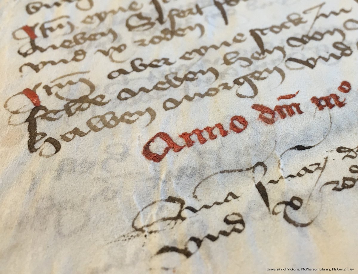 Angled, macro photo of part of a medieval manuscript, zoomed in on a Latin date in thick red ink, the surface of which crackles with age. Below are 2 lines of script in black ink. In the background, increasingly out of focus towards the top of the photo, a list of multiple items, in looping German script, in brownish ink with the first letter of each entry heightened by a red stroke. UVic, Ms.Ger.2, f. 6v.