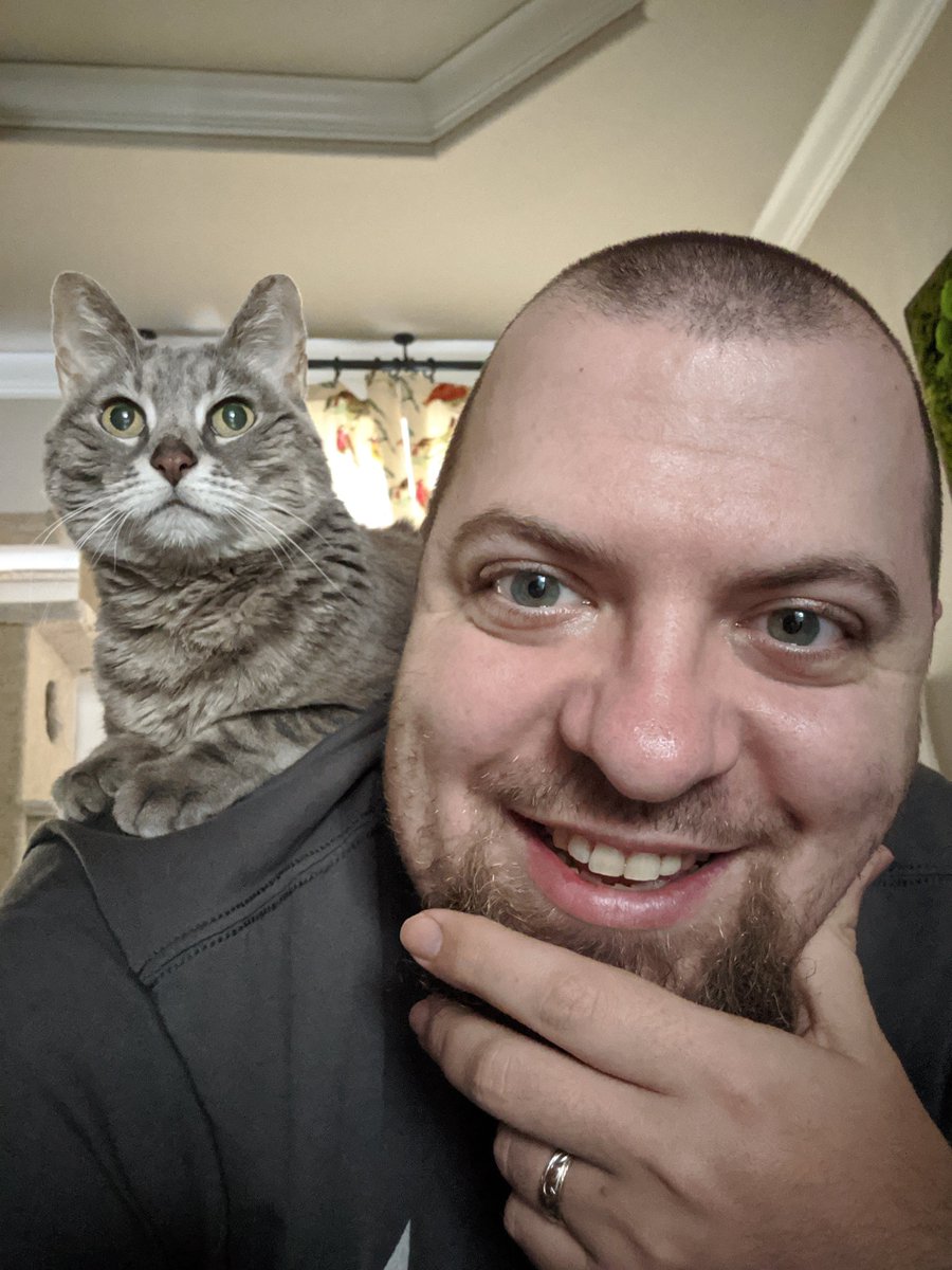 Selfie of me laying in bed on my stomach, with my cat Athena perched on my shoulder.