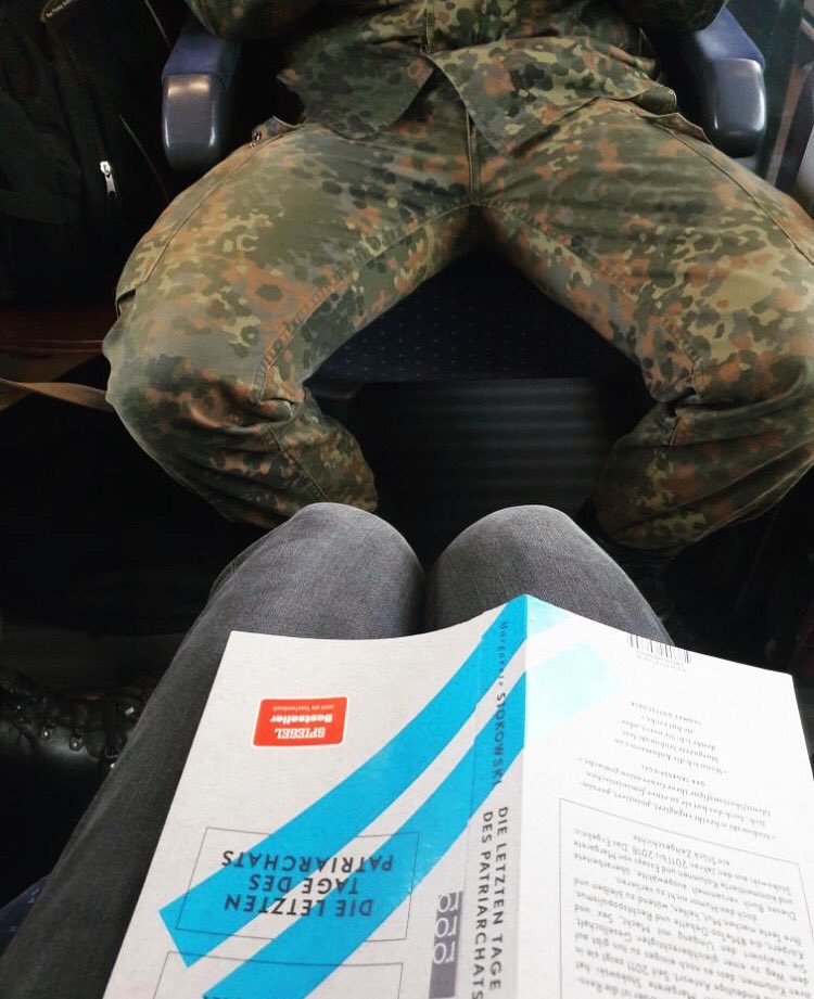 Vorne zwei Beine eng zusammen, darauf das Buch „die letzten Tage des Patriarchats“ aufgeklappt so dass man den Titel lesen kann, Gegenüber: Breitbeinig sitzender Soldat (mutmaßlich) in Uniform