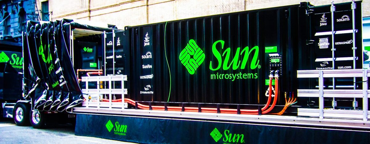 Truck with a black shipping container adorned with a Sun microsystems logo, with visible electric cables running to the container.
