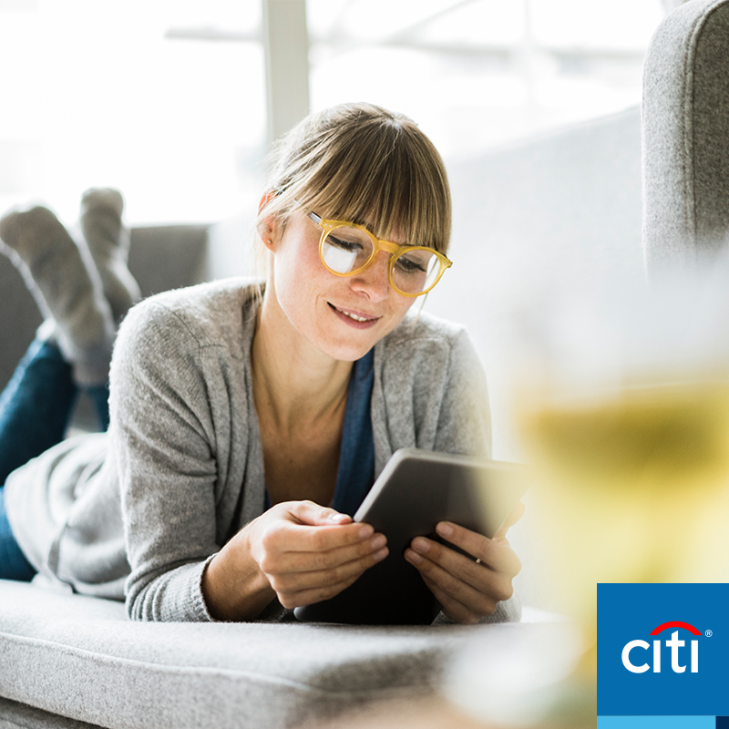 Woman with yellow glasses laying down on the couch looking at a tablet