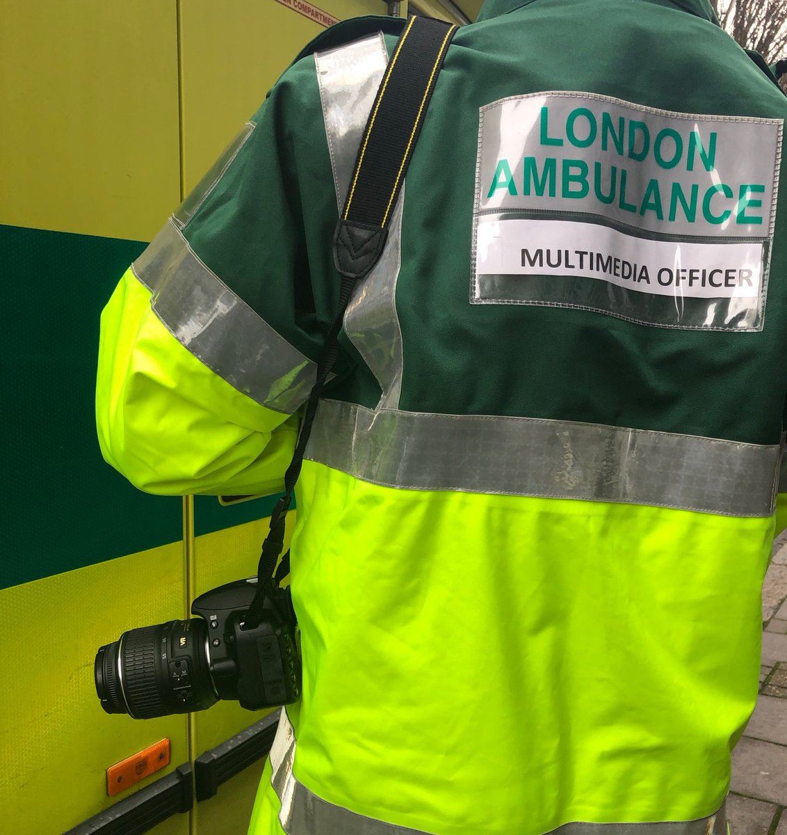 A figure with a camera on their shoulder and a hi vis jacket with the words Multimedia Officer on it