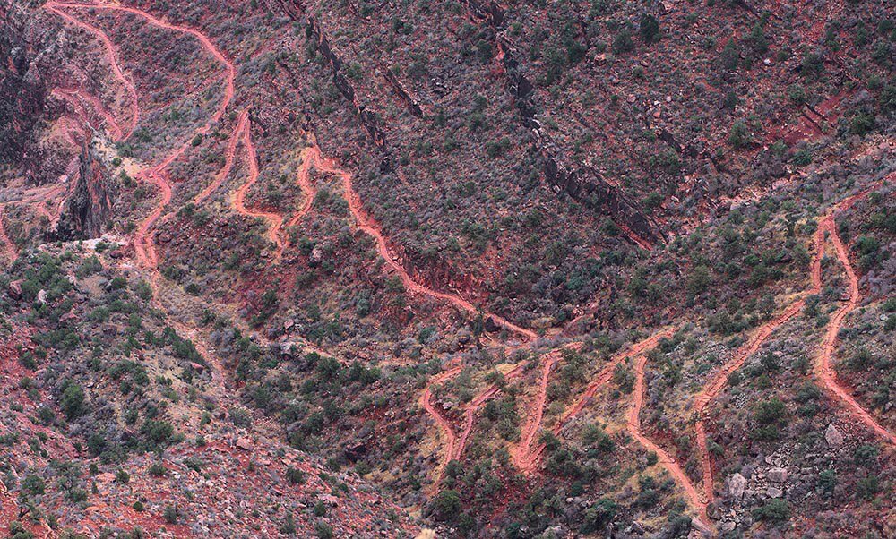 Description: a series of trail switchbacks descending a steep slope of pink colored rock. 