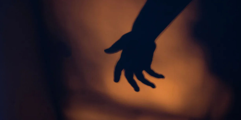 A silhouette of an outstretched hand against an amber background