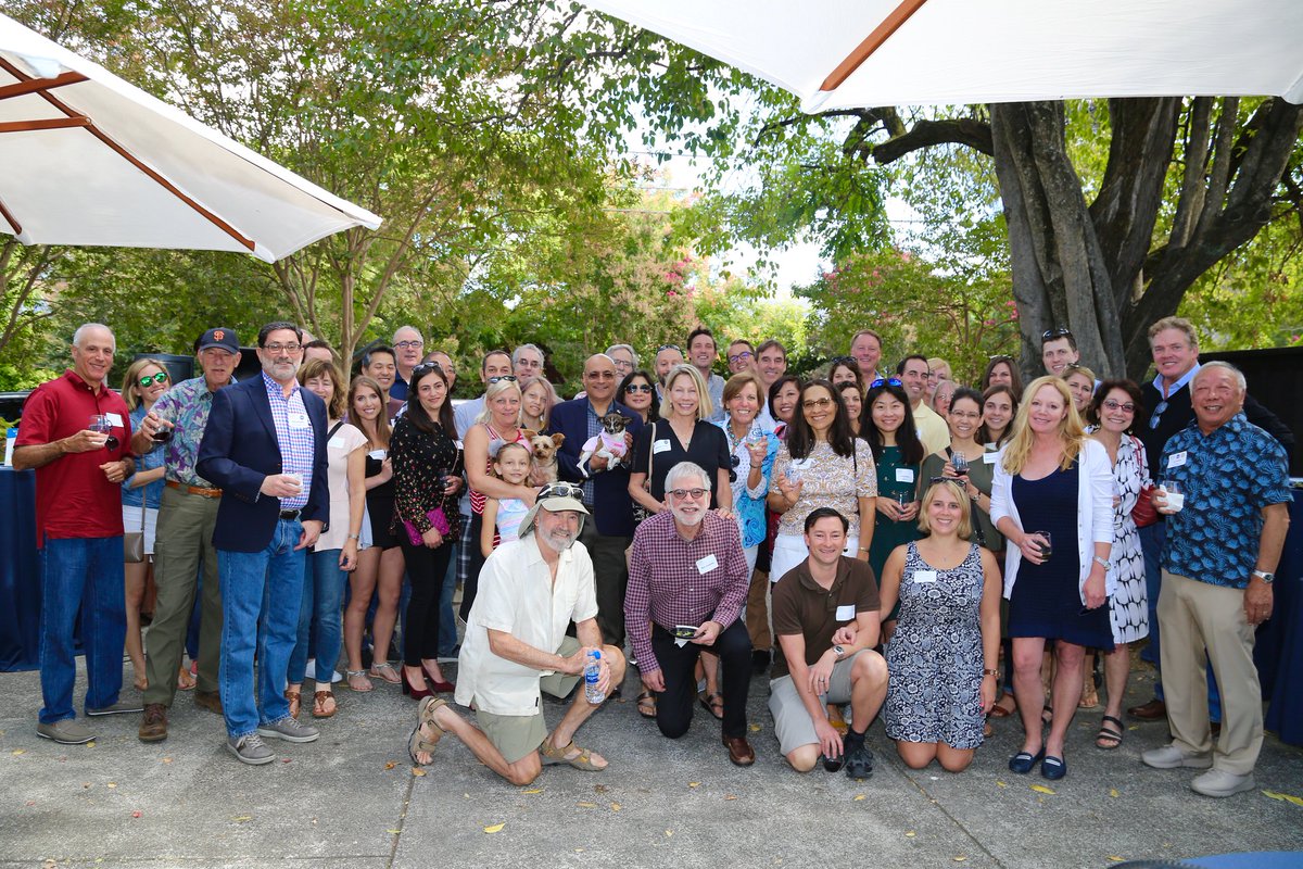 group of about 30 alumni posing and smiling in front of trees at an alumni event