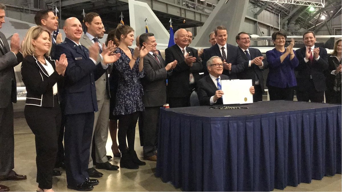 Govenor Mike DeWine, seated, displays the legislation he just signed into law, as the people behind him clap.