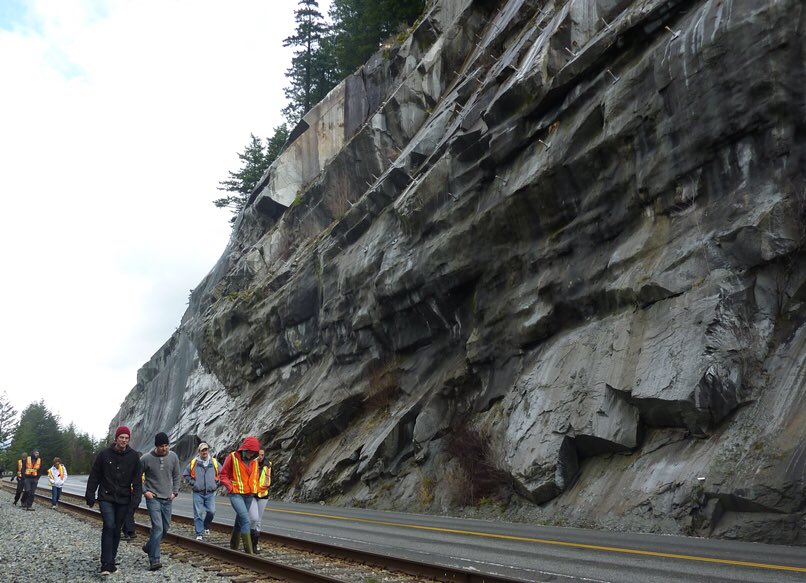 People walking along the base of a steep rock cut