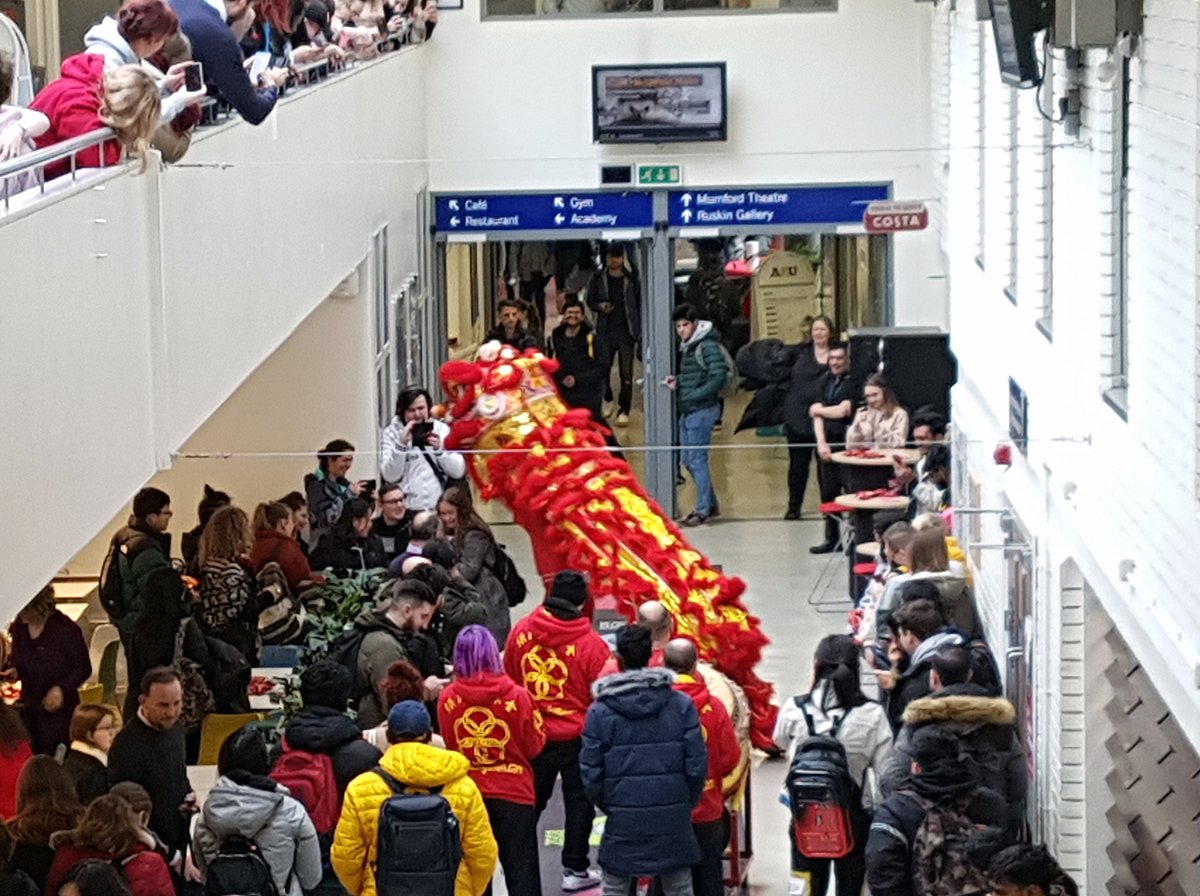 A photograph of a Chinese Dragon Dance taking place along a corridor in the Helmore Building of Anglia Ruskin University's Cambridge Campus.