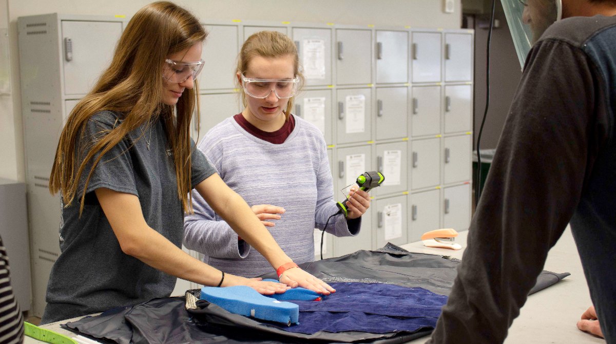 Two female students work on their prototype with power tools in a workshop during a design competition.