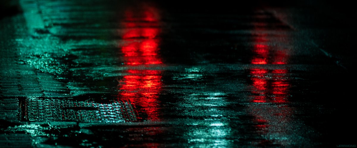Photography by Liam Wong of Tokyo at night. The red tail light streaks of a taxi cab reflecting on the road. It is red and green in color.