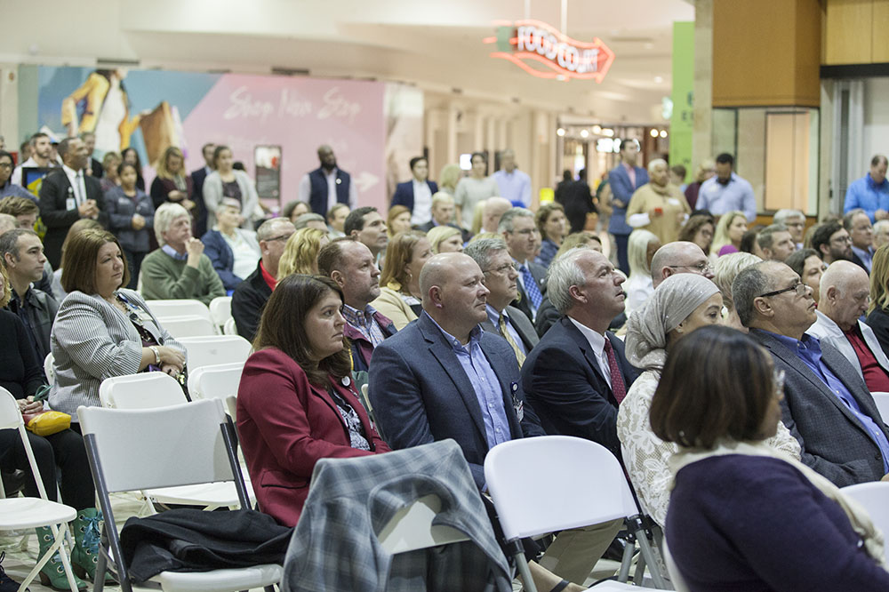People listen to speakers discussing the medical pavilion as a food court sign glows nearby.