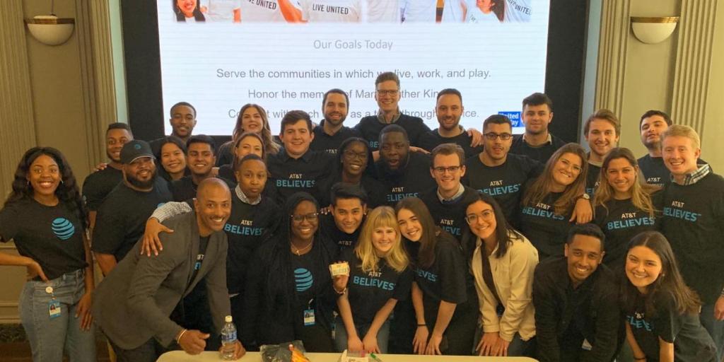 Group photo of employees wearing AT&T Believes shirts, standing in front of presentation titled, "Our Goals Today"
