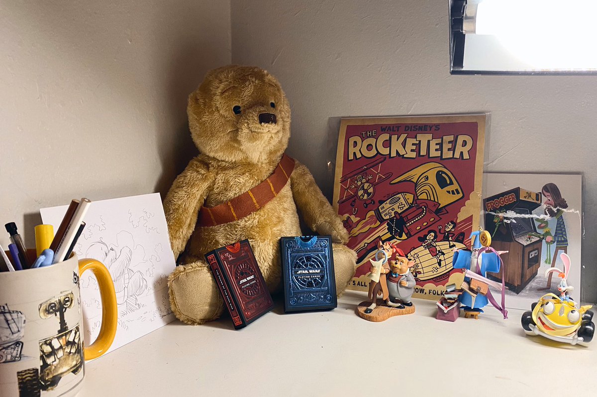 A collection of Pixar and Disney mugs, ornaments, fanart , and a Wookiee the Chew stuffed bear and pencil drawing. In a corner of my desk.