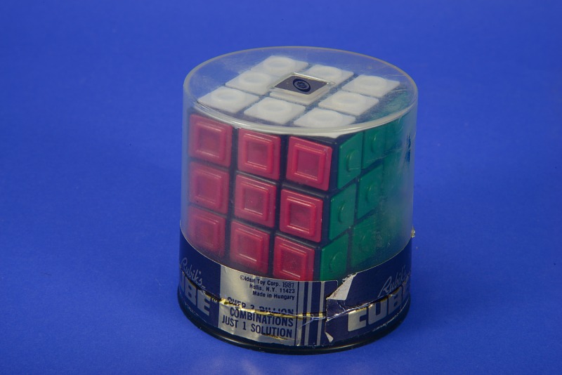 The image shows the red and green faces of a Rubiks cube still in its original packaging, although the seal has been broken.