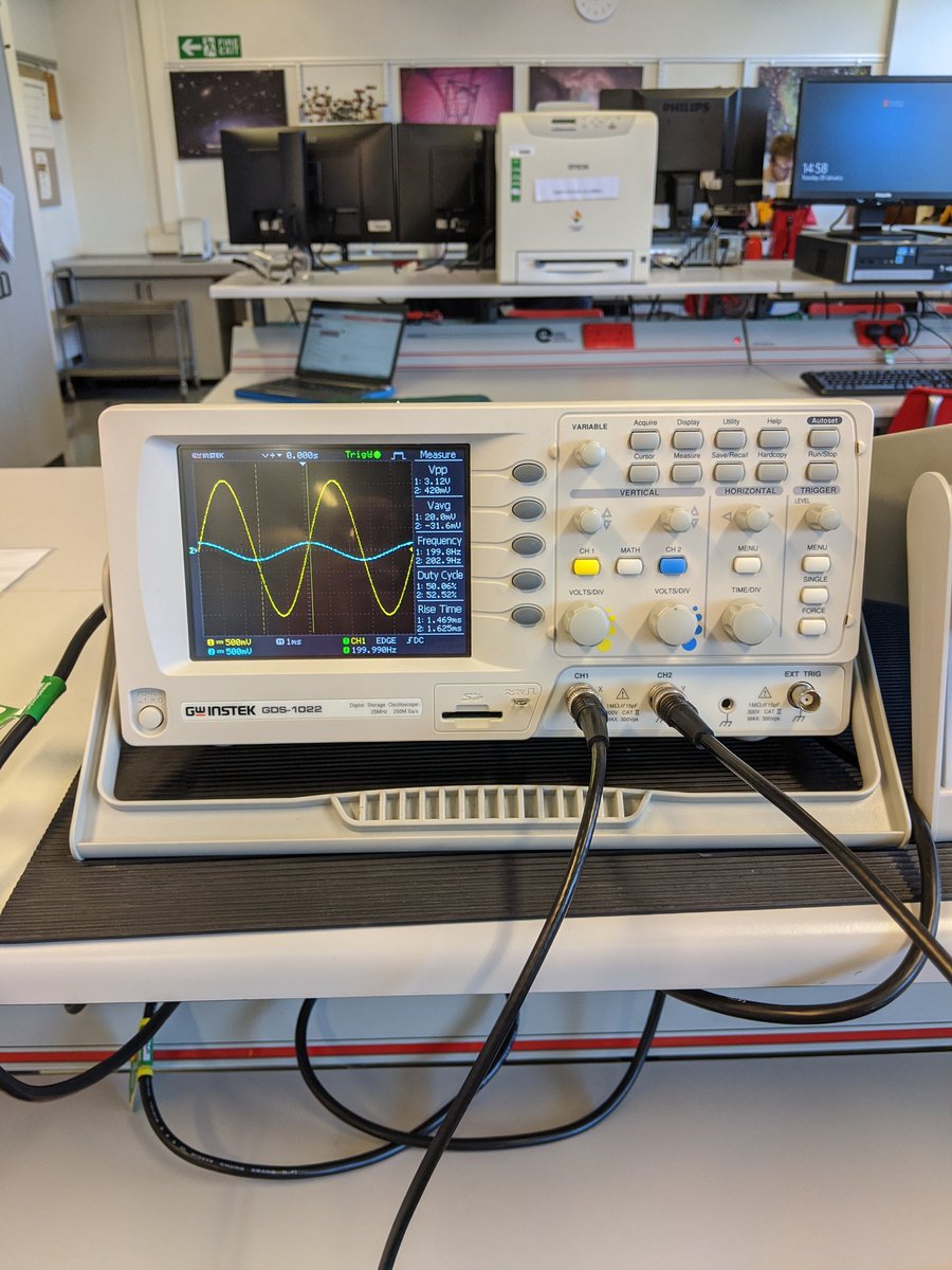 An white oscilloscope with grey, yellow and blue buttons. The black screen had a yellow and blue sine wave visible, where the blue wave has a smaller amplitude than the yellow wave.