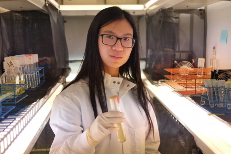 Rachel Shen is standing in a lab holding a test tube filled with liquid.