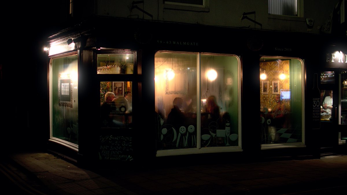 Restaurant as seen from the street; people's shadows cast against the foggy windows, warm lighting inside.