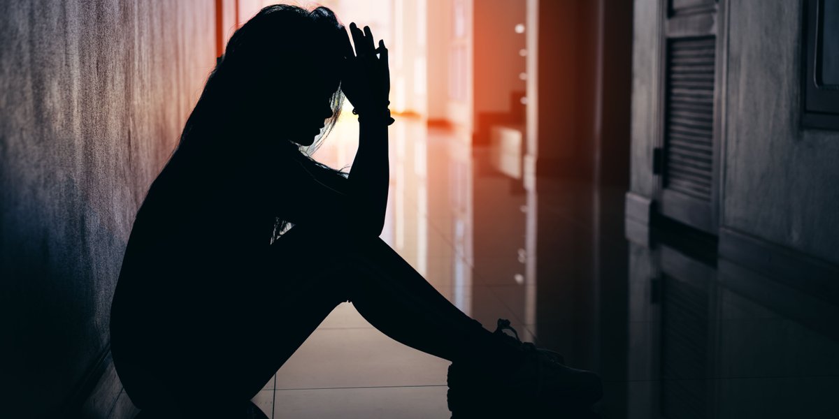 A person sitting in a hallway, holding her head between her hands.